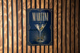 A sign with the word "MARTINI" prominently displayed, featuring an illustration of a martini glass with a green olive.