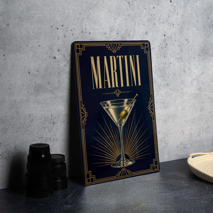 A framed image of a martini glass with an olive on the rim, placed on a gray countertop next to a stack of black camera lenses.