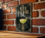 A framed poster with the text "MEZCAL LAST WORD" and an illustration of a cocktail glass on a brick wall.