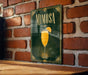 A framed poster of a mimosa cocktail is displayed on a brick wall, with a wooden table below it.