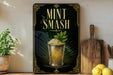 A framed poster with the text "MINT SMASH" and an illustration of a glass containing a mint-flavored beverage, surrounded by decorative elements.