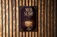 A sign for a mud slide, featuring an illustration of a glass filled with a creamy, frothy substance.