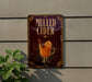 A sign advertising "Mulled Cider" is displayed on a wall, featuring an illustration of a mug filled with a warm beverage and garnished with an orange slice.