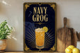 A framed poster with the text "NAVY GROG" and an illustration of a cocktail with a lemon slice. The poster is displayed on a wall next to a wooden cutting board and a potted plant.