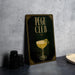 A framed poster advertising a "Pegu Club" cocktail, featuring an illustration of a cocktail glass with a lemon twist.
