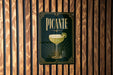 A sign for "PICANTE" cocktail is displayed on a wooden wall.