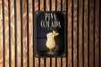 A sign for Pina Colada, featuring an illustration of a tropical drink in a glass with a straw and a pineapple on top, is displayed on a wooden wall.