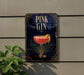 A sign for a pink gin cocktail is displayed on a wall, with a plant visible to the left.
