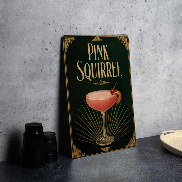 A framed poster of a pink squirrel cocktail is displayed on a wall, accompanied by a stack of black camera lenses and a white dish.