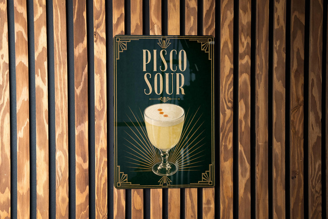 A poster with the text "Pisco Sour" and an illustration of a glass of pisco sour on a wooden wall.