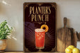 A decorative sign for "Planners Punch" is displayed on a wooden shelf, accompanied by a potted plant, a cutting board, and some lemons.