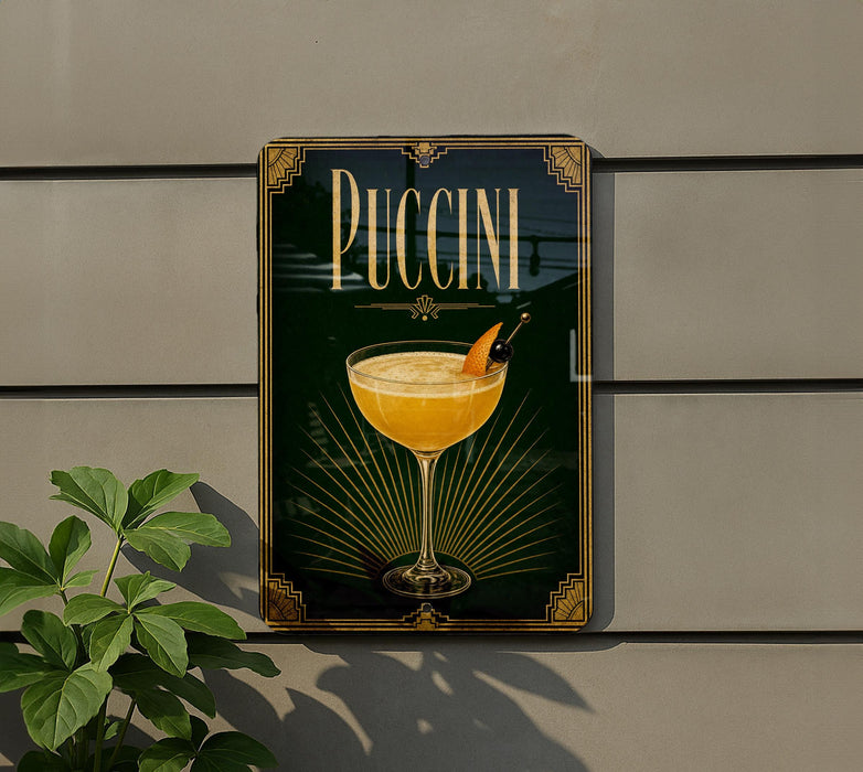 A framed poster of a Pucciini cocktail is displayed on a wall, with a plant visible to the left.