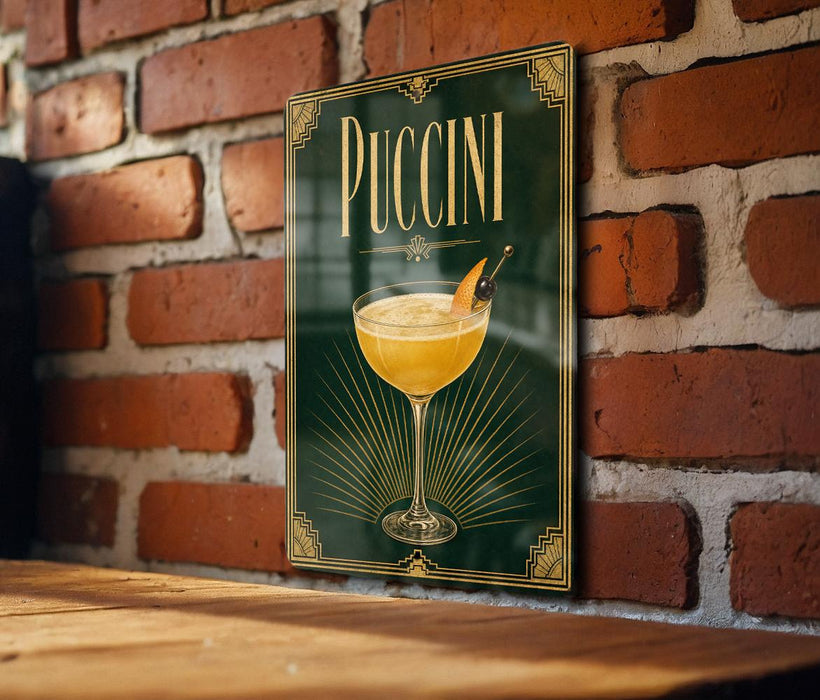 A framed poster of a Pucciini cocktail is displayed on a brick wall, with a wooden table below it.