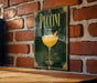 A framed poster of a Pucciini cocktail is displayed on a brick wall, with a wooden table below it.