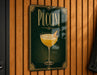 A sign for "PUCCINI" hanging on a wooden wall, featuring an illustration of a glass of Puccini cocktail.