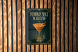 A sign for a pumpkin spice martini is displayed on a wooden wall.