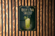 A sign for "Queen's Park Swzzle" is displayed on a wooden wall.