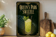 A framed advertisement for "Queen's Park Swizzle" featuring a glass of a yellow-green drink garnished with mint leaves and a straw.