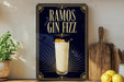 a poster advertising a drink called "RAMOS GIN FIZZ" with a glass of the drink and garnish on a wooden surface.
