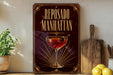 a sign for "Reposado Manhattan", which is a cocktail, placed on a wooden surface next to a cutting board and some lemons.