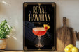 A framed poster of a Royal Hawaiian cocktail is displayed on a wall, with a wooden cutting board and a potted plant to the side.