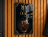 A sign that reads "RUM AND COKE" with an illustration of a glass of rum and a lime on a wooden wall.