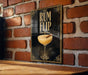 A framed poster with an illustration of a cocktail glass and the text "RUM FLIP" is displayed on a brick wall.