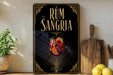 a decorative sign for "RUM SANGRIA" with a glass of wine and citrus slices, placed on a wooden surface next to a potted plant and a cutting board.