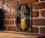 A framed poster of a cocktail called "RUM SWIZZLE" is displayed on a brick wall, featuring an illustration of a glass filled with a yellow-colored drink and garnished with a lime and a mint sprig.