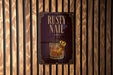 a sign that reads "RUSTY NAIL" with an illustration of a cocktail glass and a lemon slice.