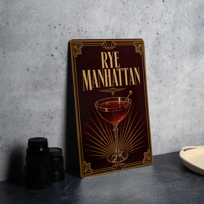A framed poster of a Manhattan cocktail is displayed on a wall, with a stack of black camera lenses and a white dish visible to the side.