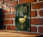 A framed poster of a cocktail glass with a cocktail in it, hanging on a brick wall.