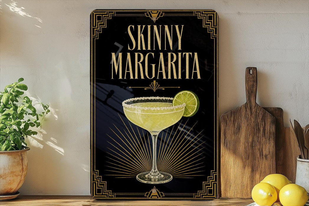A framed poster of a skinny margarita cocktail is displayed on a wall, with a wooden cutting board and a potted plant to the side.