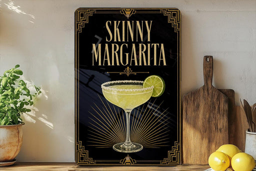 A framed poster of a skinny margarita cocktail is displayed on a wall, with a wooden cutting board and a potted plant to the side.