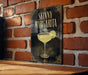 A framed poster of a skinny margarita cocktail is displayed on a brick wall.