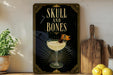 a decorative sign with the text "SKULL AND BONES" and an illustration of a cocktail glass with a skull and crossbones on the rim.