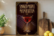 a framed poster of a smoked maple Manhattan cocktail, with a glass of the cocktail and a wooden cutting board visible.