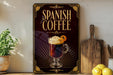 A decorative sign for Spanish coffee, featuring an illustration of a coffee drink with whipped cream and an orange slice, is displayed on a wooden shelf next to a potted plant and a cutting board.