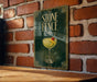 A framed poster of a cocktail with a cherry on top, hanging on a brick wall.