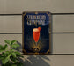A sign for a strawberry champagne drink is displayed on a wall, with a plant visible to the left.