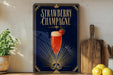 A framed poster of a strawberry champagne drink is displayed on a wall, with a wooden cutting board and a potted plant to the side.