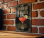 A framed poster of a strawberry margarita is displayed on a brick wall.