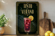 a framed advertisement for a drink called "Tinto de Verano", which is a red cocktail with a lemon slice. The advertisement has a black background with gold accents, and the drink is depicted in a glass with ice cubes.
