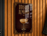 A sign that reads "Toasted Almond" with an illustration of a cocktail on it, mounted on a wooden wall.