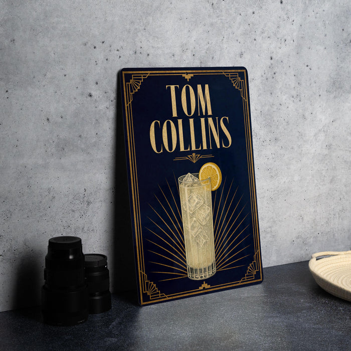 A framed poster of a cocktail with a lemon slice, featuring the name "Tom Collins" on the poster.