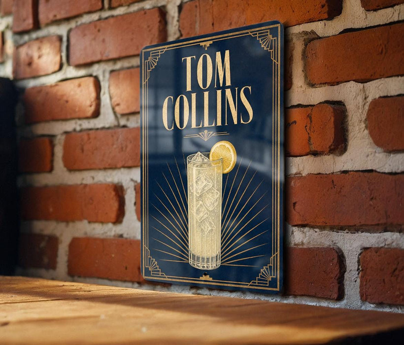 A sign for a cocktail named "Tom Collins" is displayed on a brick wall, featuring an illustration of a cocktail glass with a lemon slice.