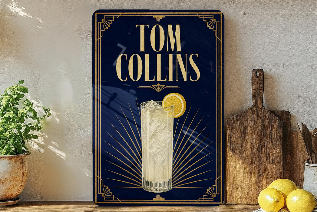 A framed advertisement for Tom Collins cocktails, featuring a glass of the drink and a lemon slice, is displayed on a wall next to a wooden cutting board and a potted plant.