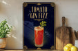 A framed advertisement for a tomato gin fizz cocktail, featuring a glass of the drink with a garnish and a wooden cutting board on a kitchen counter.