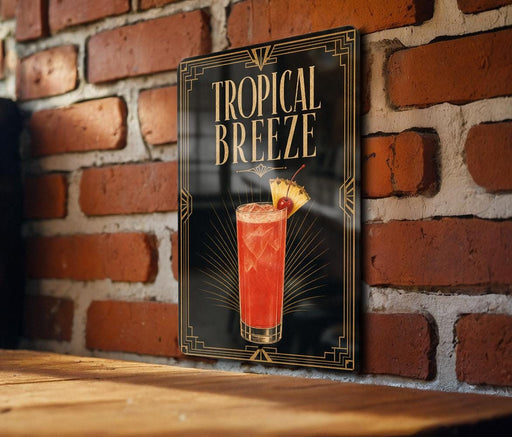 A framed poster of a tropical breeze cocktail hangs on a brick wall, featuring a vibrant red drink with a slice of pineapple and a cherry on top.