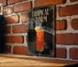 A framed poster of a tropical storm cocktail is displayed on a brick wall.